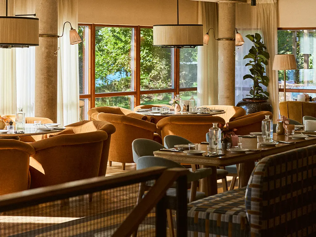 Interiör av Restaurant Palmers med mjuka fåtöljer, dukade bord och stora fönster med utsikt mot grönska.