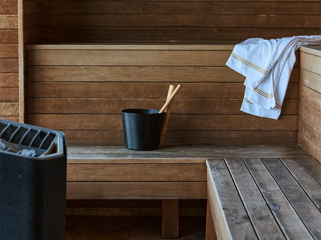 Träinteriör i en bastu med vattenhink, skopa och handduk på Ellery Beach House.
